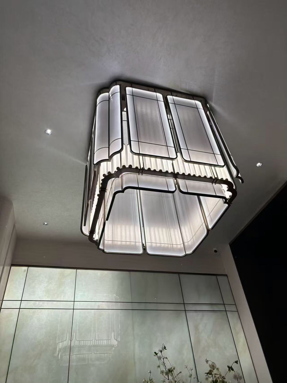 Celestia Frame chandelier installed in modern double height interior Contemporary geometric chandelier with soft ambient lighting Modern architectural ceiling chandelier with framed design Luxury rectangular chandelier for foyer installation Designer LED chandelier with structured metal frame Minimal modern chandelier illuminating luxury interior space